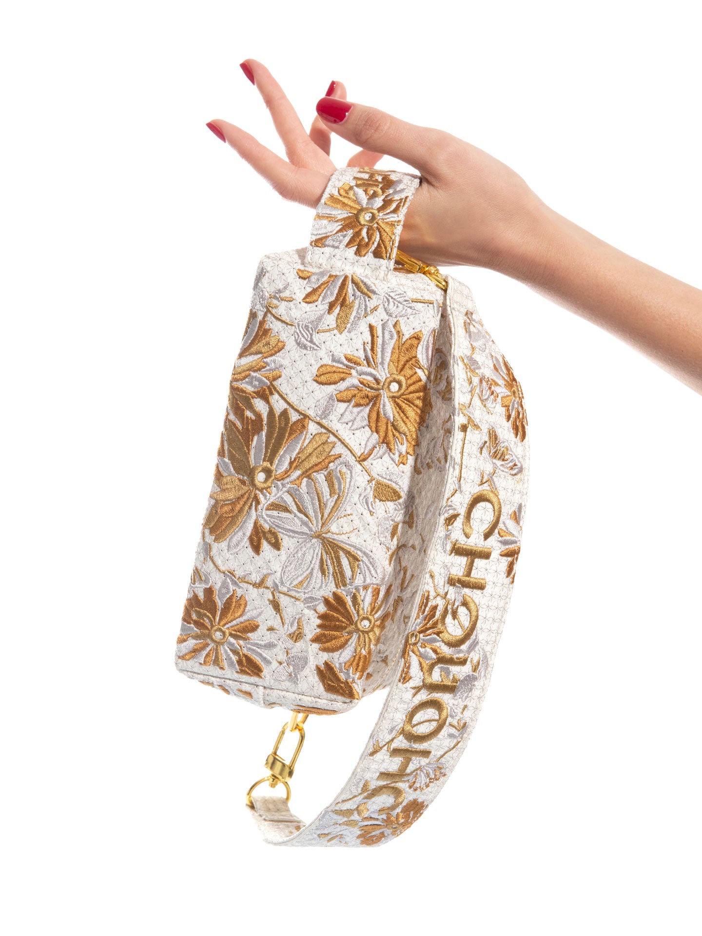 Elegant red-manicured hand holding CHOUCHOU TOKYO’s signature white pouch with silver and gold floral embroidery. A refined accessory with delicate, high-end detail.